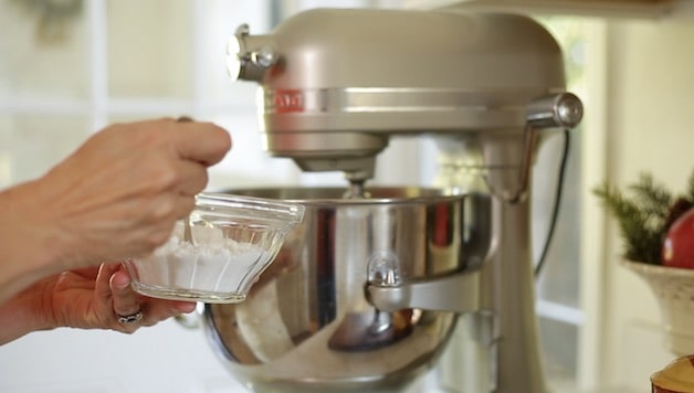 Adding spoonfuls of confectioner's sugar to a bowl of an electric mixer