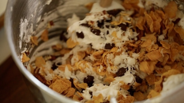 Bowl of stiff egg whites being mixed with chocolate chips, cornflakes, nuts and coconut