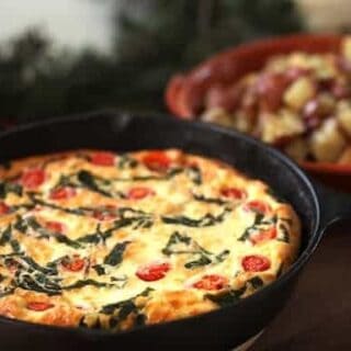 Tomato, Basil and CHeese Frittata in a cast iron skillet with roasted potatoes in the background