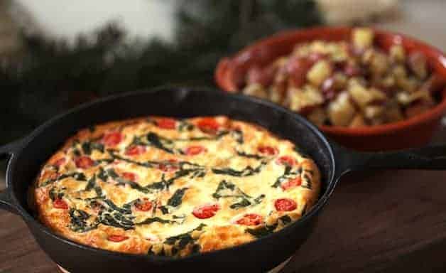 Tomato, Basil and CHeese Frittata in a cast iron skillet with roasted potatoes in the background