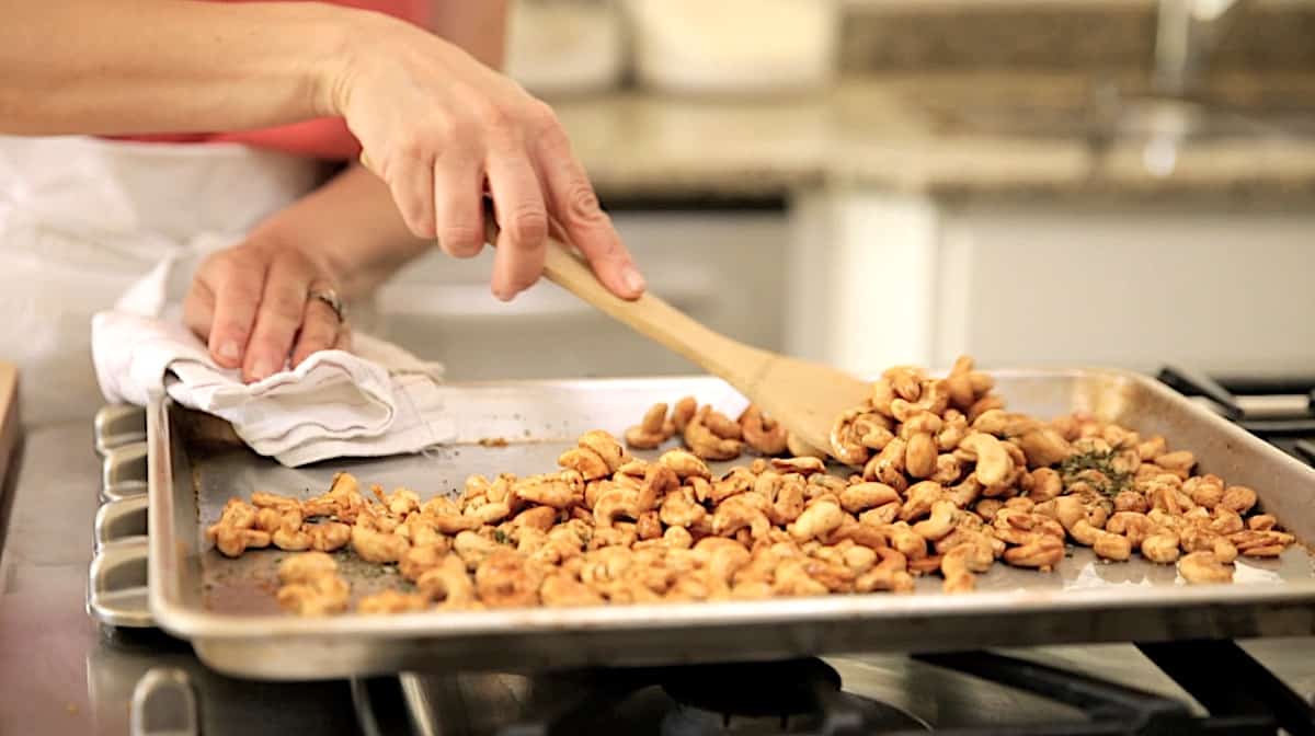 a person tossing cooling cashews on a baking sheet