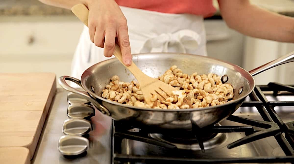a person coating cashews in sauce in a skillet