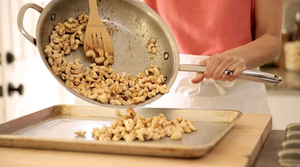 Cashews being transfers from a skillet to a baking sheet