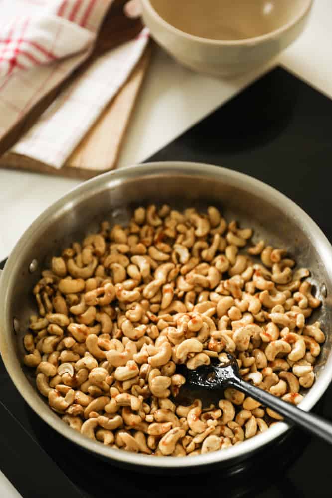 cashews in a skillet being coated with a honey butter mixture.