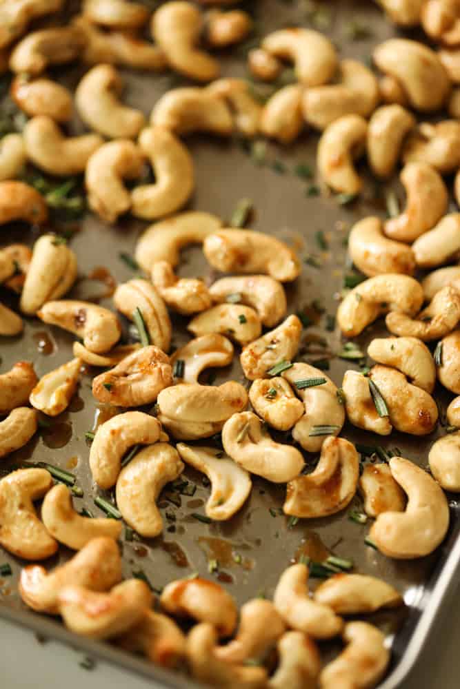 raw cashews on a baking tray tossed with a honey butter syrup and fresh rosemary.