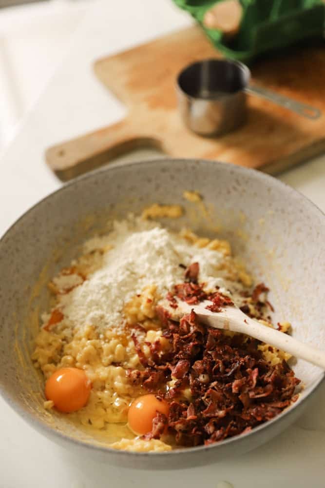 Macaroni, eggs, flour and cooked bacon in a mixing bowl.