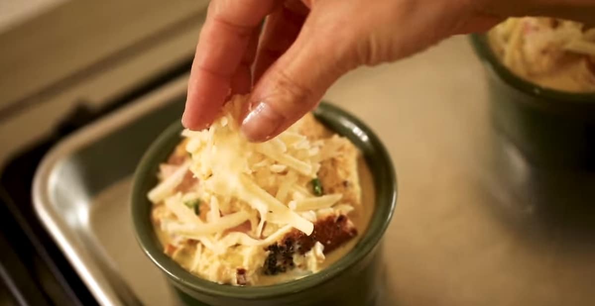 a person placing grated cheese on top of a egg bake ramekin