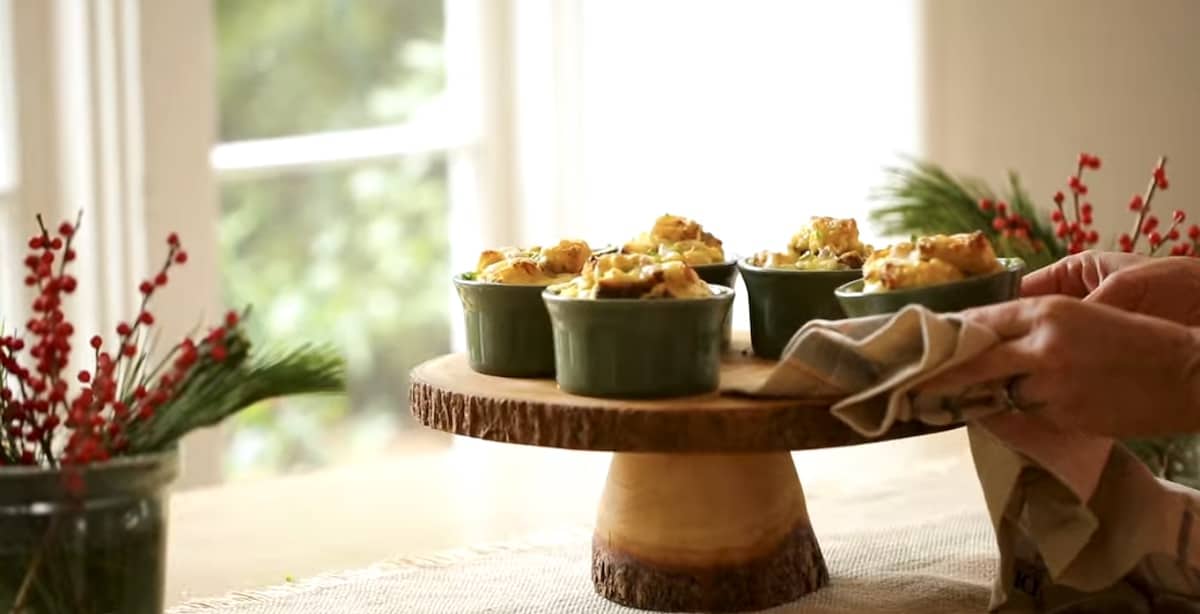 a person placing a mini egg bake in a ramekin on a cake stand with other mini egg bakes