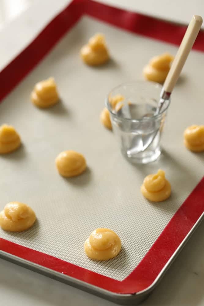 flattening the peaks of choux pastry mounds with water and a spoon on a baking tray.