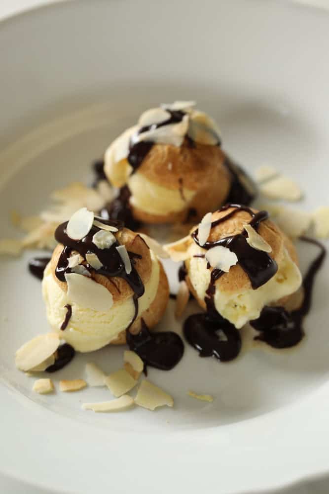 fully assembled profiteroles in a white bowl.