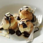 Choux Pastry filled with ice cream and topped with chocolate sauce and toasted almonds in a white bowl.
