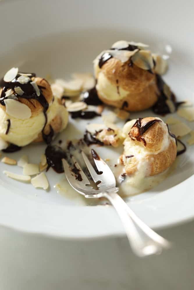 three assembled choux pastry sheels with ice cream and chocolate sauce with a bite taken out of it.