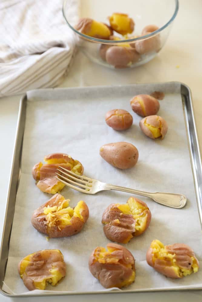 Boiled potatoes on a baking sheet being smashed with a fork.