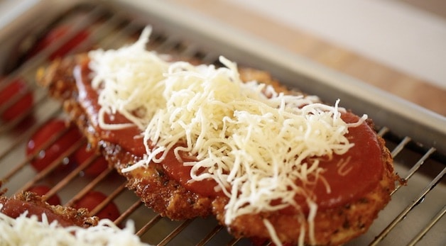 Tight shot of shredded mozzarella cheese on a breaded chicken cutlet with tomato sauce