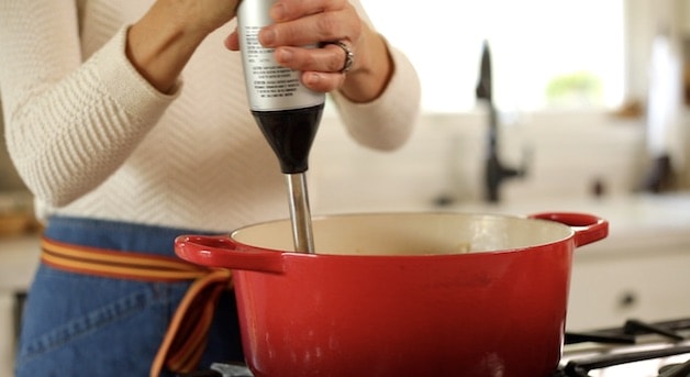Blending soup with an immersion blender in a red pot