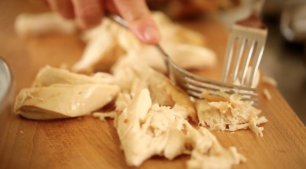 Shredding chicken with forks on a cutting board