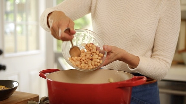 Cannellini beans being added to white chicken chili simmering in a red pot