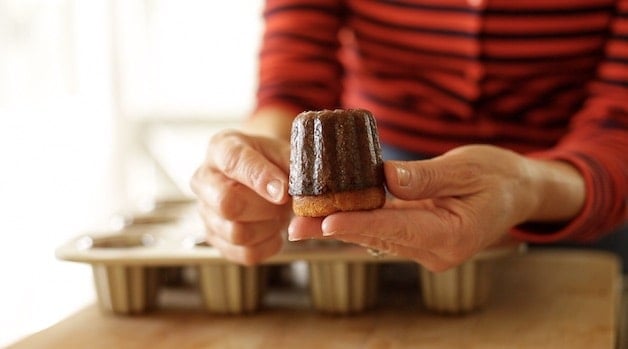 Holding up a freshly baked canele that is beautifully caramelized with a hard exterior