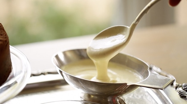 Creme Anglaise in a silver gravy boat being lifted out with a silver spoon