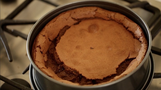 a sunken and cracked flourless chocolate cake in a cheesecake pan resting on a cooktop