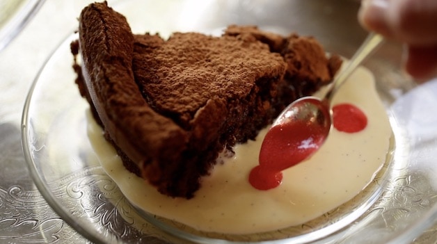 Slice of flourless chocolate cake in a pool of creme anglaise with dollops of raspberry juice