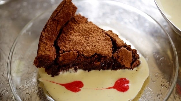 A slice of Flourless Chocolate Cake in a pool of creme anglaise with raspberry coulis hearts