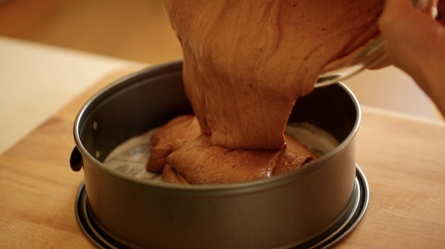 pouring flourless chocolate cake batter into a prepared cheesecake pan