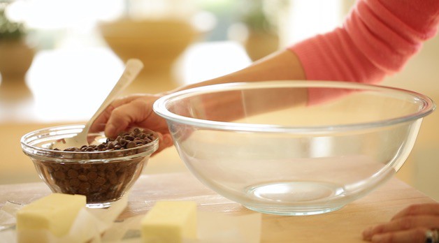 Clear bowl with chocolate chips and butter on a cutting board