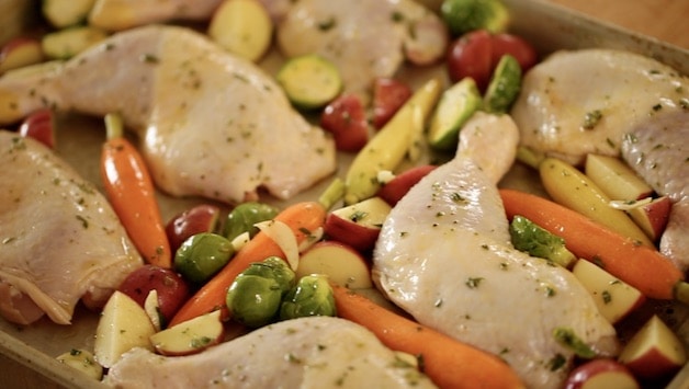 raw chicken legs and veggies on a sheet pan covered with oil and herbs