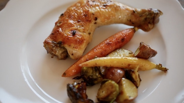a white plate with a roasted chicken leg and roasted baby veggies