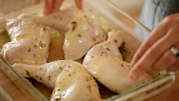 chicken legs in a casserole dish being covered with olive oil marinnade