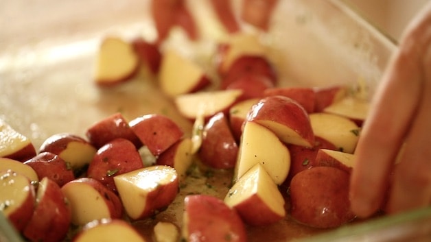 tossing quartered red potatoes in olive oil marinade for a sheet pan dinner