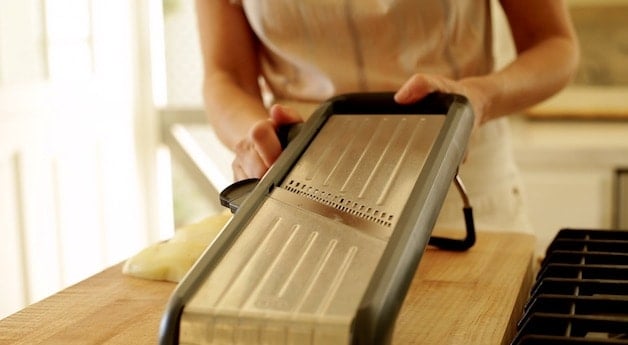 A person setting the thickness of a mandoline slicer