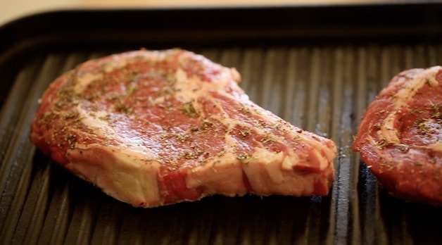 A close up of a ribeye steak grilling on a grill pan