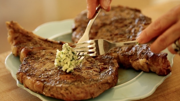 adding a dollop of Herb butter to a ribeye steak on a blue plate