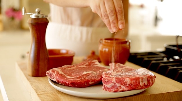 salting 2 Rib Eye Steaks on a plate