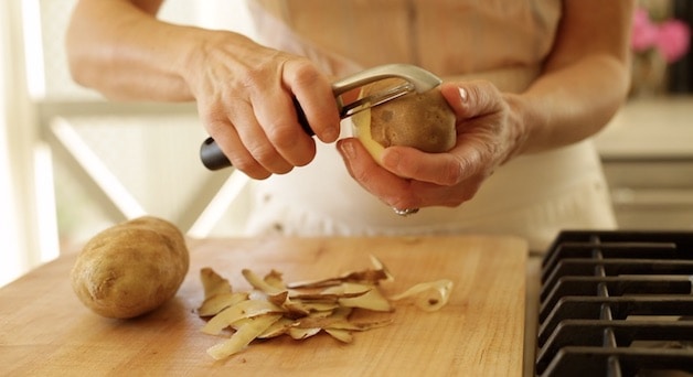 peeling a russet potato with a potato peeler over a cutting board