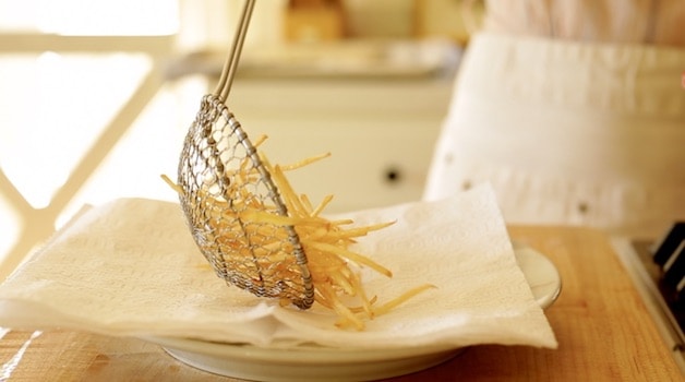A spider strainer placing fried French Fries on a plate lined with paper towels