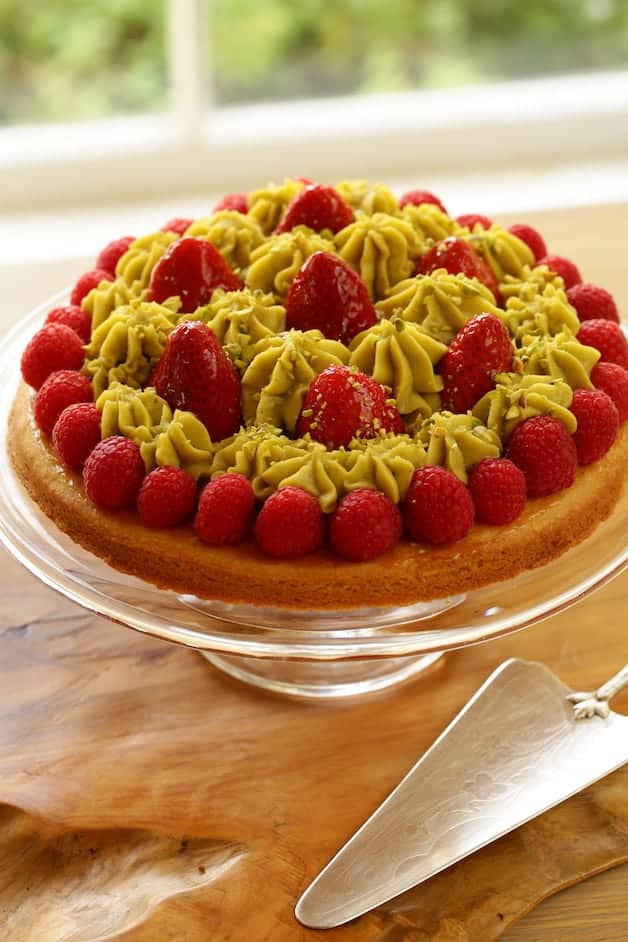 Strawberry Pistachio tart on a cake stand with silver server