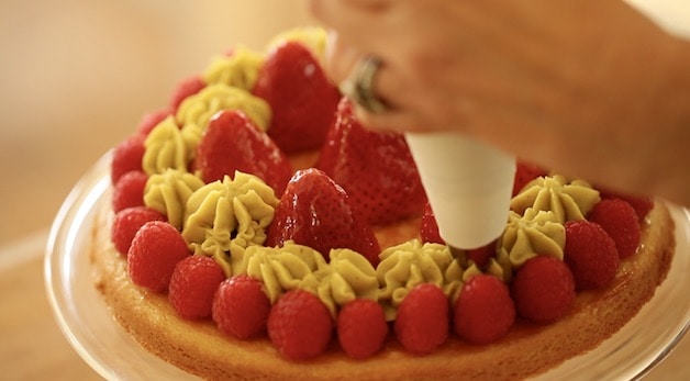 pipping pistchio pastry cream in between strawberries on a tart base