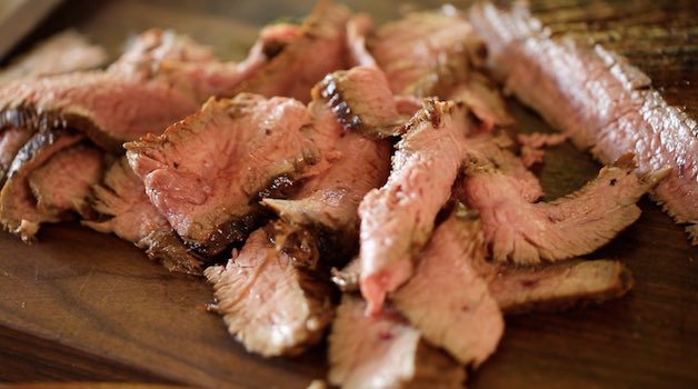 Sliced Flank Steak on a dark cutting board ready for tacos