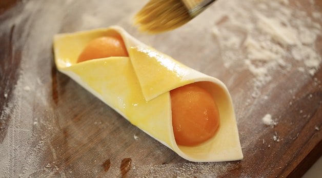 Tight shot of an apricot pastry wrapped and sealed brushed with egg wash