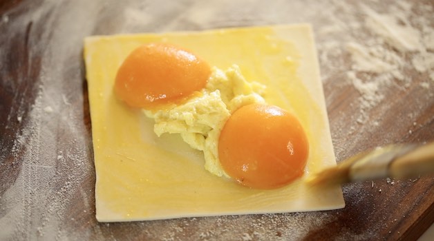 Apricots on top of pastry cream on a puff pastry square on a cutting board