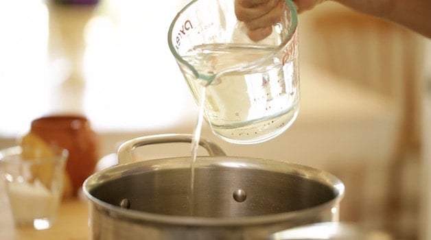 Adding water from a glass pitcher into a pot on a cooktop