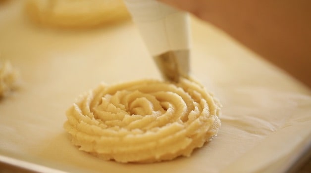 Tight shot of churro dough being pipped from a pastry bag