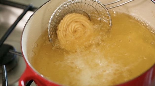 Frying churro disk in a hot pot of oil with a spider strainer