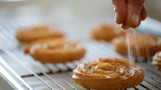 Sprinkling cinnamon sugar on a fried churro disk