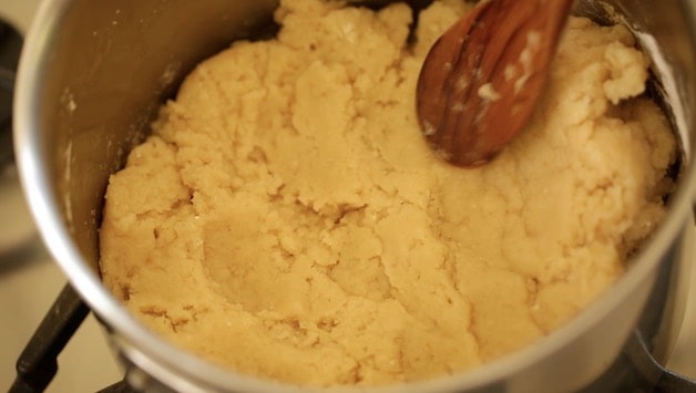 Flattening dough in a pot before adding egg to churro dough