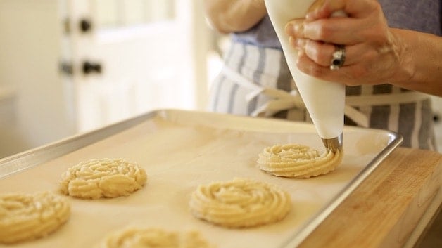 piping churron dough onto parchment lined cookie sheets from a pastry bag