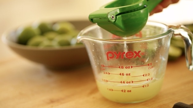 squeezing key limes into a measuring pitcher with a green lime squeezer